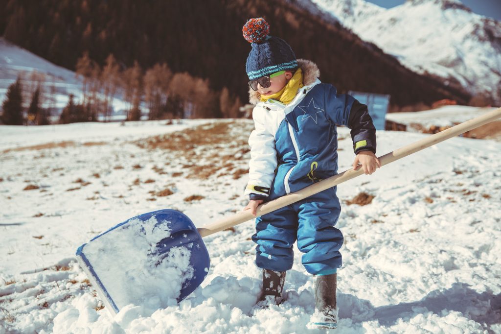 Kid shovelling snow with a big blue shovel